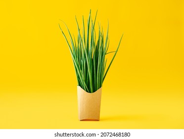 Fresh green onions in fast food paper box on bright yellow background. Healthy eating concept