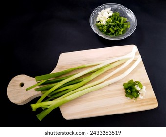 Fresh green onions or spring onions on wooden board, isolated on black background. concept of cutting spring onions on a wooden cutting board - Powered by Shutterstock