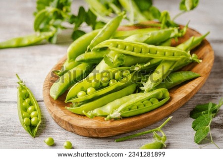 Fresh green peas in wooden bowl with pods and leaves on white wooden table, healthy green vegetable or legume
