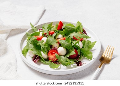 Fresh green salad made with mozzarella cheese, cherry tomatoes, arugula and olive oil on white stone table background. Healthy food and diet concept. Flat lay, copy space. - Powered by Shutterstock