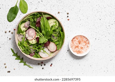 Fresh green salad with mix of salad leaves, small radish, onion and cucumbers on white marble background. Healthy diet food concept. 