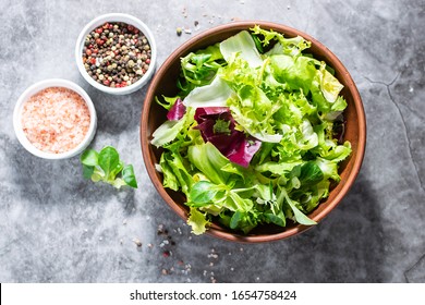 Fresh Green Salad Mix With Olive Oil And Himalaya Salt On Dark Stone Table Top View. Healthy Food Concept.