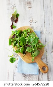 Fresh Green Salad With Spinach, Arugula, Romaine And Lettuce On A Wooden Chopping Board On Rustic White Background, Top View