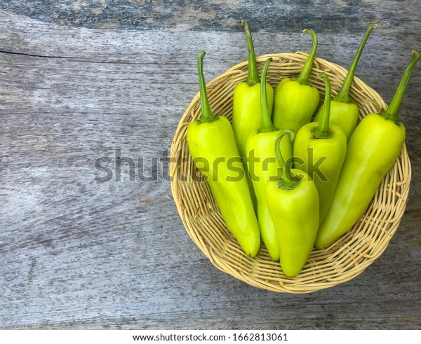 fresh green sweet peppers (banana peppers) in\
bamboo basket on wooden\
table.