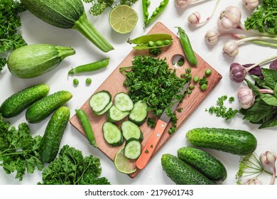Fresh green vegatables and cutting board on a white background. Cucumbers, garlic, green pea, parsley, basil, zucchini. Fresh green produce. Top view.