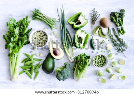 Fresh green vegetables variety on rustic white background from overhead, broccoli, celery, avocado, brussel sprouts, kiwi, pepper, peas, beans, lettuce,