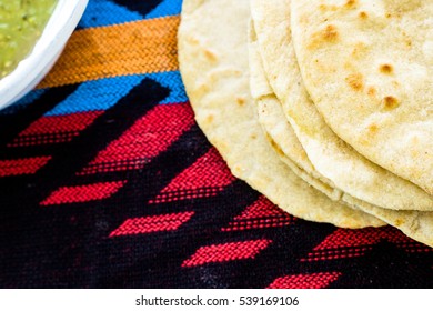 Fresh, handmade flour tortillas on Aztec surface with white rim of dish and green salsa.