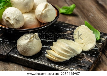fresh handmade soft Italian cheese with fresh basil leaves from Puglia, white balls of burrata or burratina cheese made from mozzarella and cream filling on a wooden board,