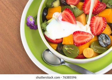 Fresh and healthy fruit salad with strawberry, kiwi, grape, mango and physalis in a bowl with plain yogurt being poured over