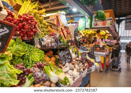 Fresh, healthy greens, vegetables, and fruits on a farmers market stall. The stall features salad leaves, radishes, oranges, mushrooms, artichokes, and a variety of other veggies in a European market.