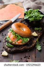 Fresh Healthy Organic Sandwich With Bagel And Salmon, Cream Cheese And Wild Rocket On Chopping Board With Smoked Salmon Pack On Wooden Background.