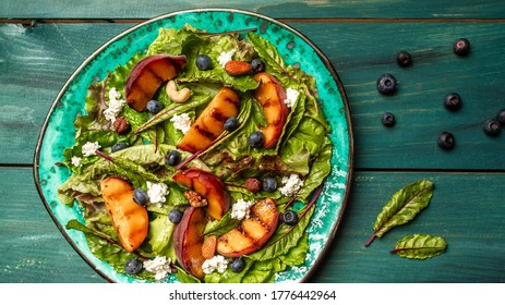 Fresh Healthy Salad With Grilled Peaches, Blueberries, Nuts And Goat Cheese On Wooden Table. Top View, Overhead, Banner.