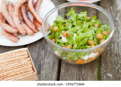 Fresh Healthy Salad With Olives And Feta Chees On Wooden Table. Baked Crisps With Sausages At The Picnic Time. Tasty Fresh Food