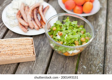 Fresh Healthy Salad With Olives And Feta Chees On Wooden Table. Baked Crisps With Sausages At The Picnic Time. Tasty Fresh Food