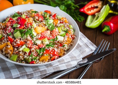 Fresh healthy salad with quinoa, colorful tomatoes, sweet pepper, cucumber and parsley on wooden background close up. Food and health. Superfood.