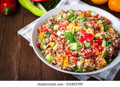 Fresh healthy salad with quinoa, colorful tomatoes, sweet pepper, cucumber and parsley on wooden background close up. Food and health. Superfood meal. Clean eating