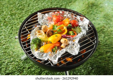 Fresh Healthy Selection Of Grilled Vegetables Cooked In Foil Over A BBQ Including Broccoli, Peas, Onion, Sweet Pepper, Mushroom, And Tomato