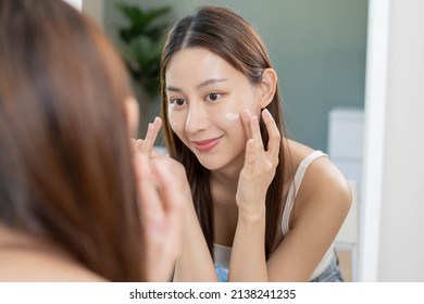 Fresh healthy skin, beautiful smile of asian young woman, girl looking at mirror, applying moisturizer on her face, putting cream treatment before makeup cosmetic routine at home. Facial Beauty. - Shutterstock ID 2138241235