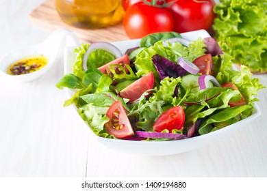 Fresh healthy vegetable salad made of cherry tomato, ruccola, arugula, feta, olives, cucumbers, onion and spices. Greek, Caesar salad in a  bowl on wooden background. Healthy organic diet food concept