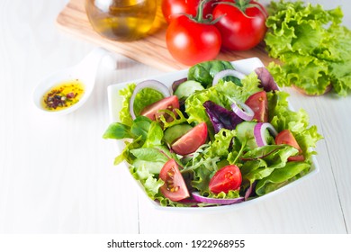 Fresh healthy vegetable salad made of cherry tomato, ruccola, arugula, feta, olives, cucumbers, onion and spices. Greek, Caesar salad in a white bowl on wooden background. 