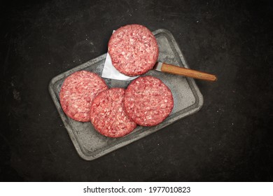 Fresh Home Made Beef Steak Burgers And Spatula On Finnish Fire Stone Slate For Grilling And Serving Hot Dishes. Raw Steak Burgers Cutlets And Grill Tools Overhead View. Burgers For BBQ Grill, Top View