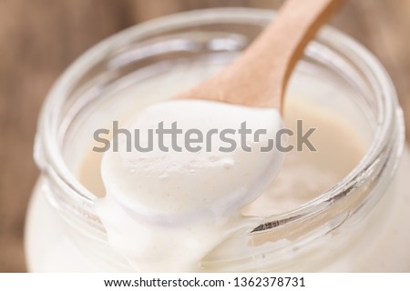 Fresh homemade bubbly sourdough starter, fermented mixture of water and flour to use as leaven for bread baking, on wooden spoon placed on rim of glass jar (Selective Focus one third into the spoon) 