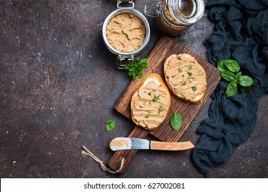 Fresh homemade chicken liver pate on bread over rustic background, top view