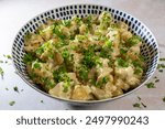 Fresh homemade creamy potato salad, seasoned with finely chopped fresh parsley, made with new baby potatoes of the Gemson variety, served in a large bowl.