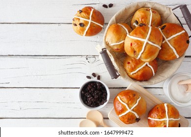 Fresh homemade Hot Cross Buns. Overhead view side border on a white wood background with copy space.