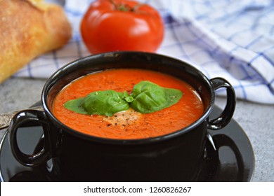 Fresh Homemade Italian Tomato Soup With Basil And A Dollop Of Sour Cream In A Soup Pot With An Italian Bread Roll And A Tomato On A Stone Surface