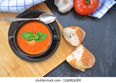 Fresh Homemade Italian Tomato Soup With Basil And A Dollop Of Sour Cream In A Soup Pot With An Italian Bread Roll And A Tomato On A Stone Surface