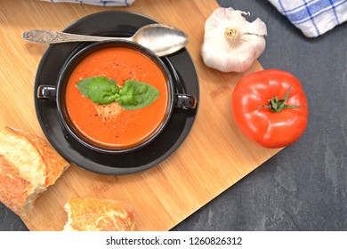 Fresh Homemade Italian Tomato Soup With Basil And A Dollop Of Sour Cream In A Soup Pot With An Italian Bread Roll And A Tomato On A Stone Surface