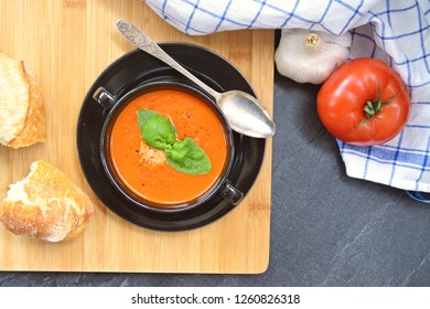 Fresh Homemade Italian Tomato Soup With Basil And A Dollop Of Sour Cream In A Soup Pot With An Italian Bread Roll And A Tomato On A Stone Surface