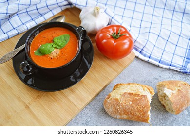 Fresh Homemade Italian Tomato Soup With Basil And A Dollop Of Sour Cream In A Soup Pot With An Italian Bread Roll And A Tomato On A Stone Surface