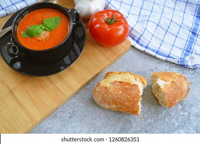 Fresh Homemade Italian Tomato Soup With Basil And A Dollop Of Sour Cream In A Soup Pot With An Italian Bread Roll And A Tomato On A Stone Surface