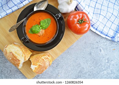 Fresh Homemade Italian Tomato Soup With Basil And A Dollop Of Sour Cream In A Soup Pot With An Italian Bread Roll And A Tomato On A Stone Surface