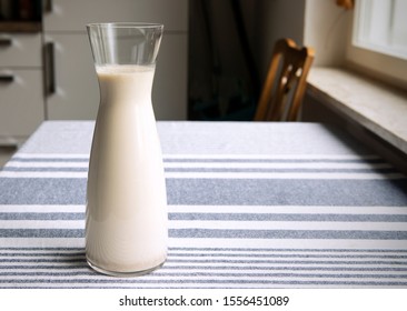 Fresh homemade oat milk in glass carafe standing on the kitchen table. Cozy atmosphere of interior, simply, plain healthy plant milk.Copy space.