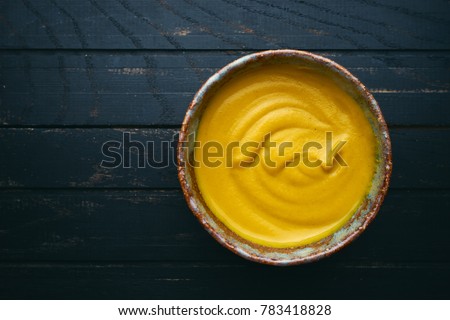 Fresh homemade organic mustard in bowl on wooden background top view