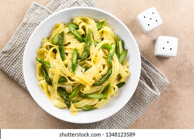 Fresh Homemade Pasta Dish Of Fettuccine Or Tagliatelle, Green Asparagus, Garlic And Lemon Juice In Bowl, Ground Black Pepper On The Top, Salt And Pepper Shaker On The Side, Photographed Overhead