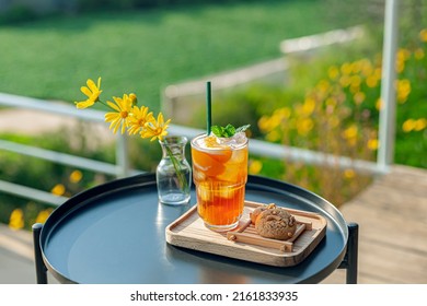 Fresh Homemade Peach Ice Tea With Mint, Chocolate Chip Cookie Served On Table Outdoors. Summer Cold Fruit Drink In Sunny Afternoon With Yellow Flowers Behind