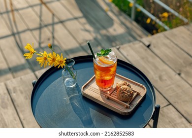 Fresh Homemade Peach Ice Tea With Mint, Chocolate Chip Cookie Served On Table Outdoors. Summer Cold Fruit Drink In Sunny Afternoon With Yellow Flowers Behind