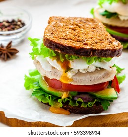 Fresh Homemade Sandwich With Cereals Dark Rye Grain Bread, Salad Lettuce, Avocado, Tomato, Grilled Chicken Breast, Curd Cheese, Poached Egg And Greengrocery On Paper. Healthy Lifestyle Breakfast. 