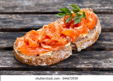 Fresh homemade sandwich with salmon on old wooden table.