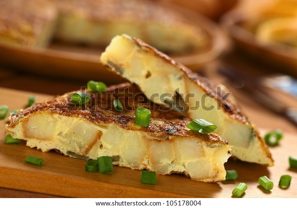 Fresh homemade Spanish tortilla (omelette with\
potatoes and onions) slices with scallion on top on wooden cutting\
board (Selective Focus, Focus on the front upper edge of the lower\
tortilla slice)