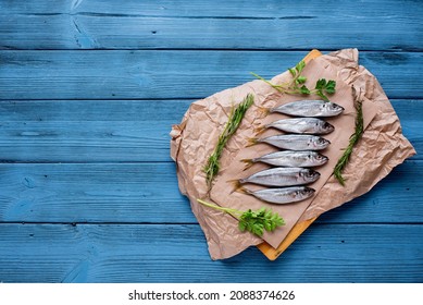 Fresh horse mackerel fish lies on paper on a blue wooden background, greenery is laid out next to it