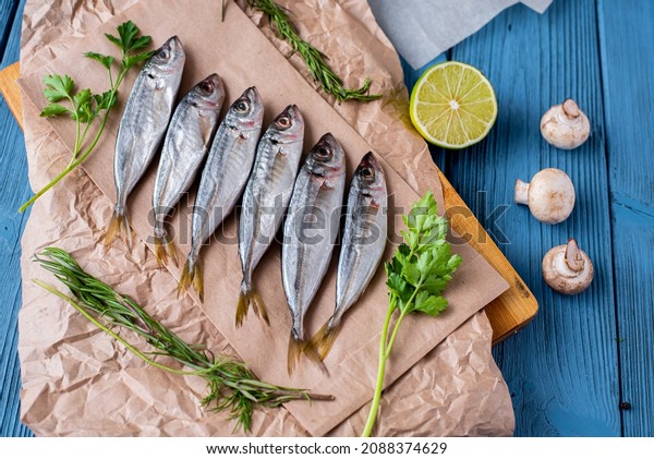 Fresh
horse mackerel fish top view on paper and wooden blue background,
mushrooms, greens and lime are laid out next to
it