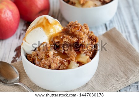 Fresh hot homemade apple crisp or crumble with crunchy streusel topping topped with vanilla bean ice cream and Caramel Sauce. Selective focus with blurred background. 