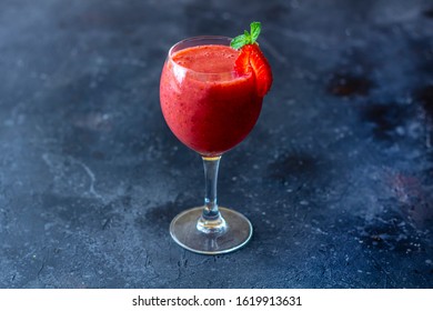 Fresh Iced Strawberry Smoothie In Wine Glass Decorated With Slice Of Strawberry And Mint On A Dark Background. Summer Slushy Drink. Close Up, Copy Space For Text.