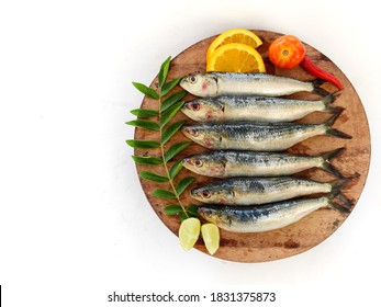 Fresh Indian Sardine Fish Decorated With Curry Leaves ,Lemon Slice And Tomatoes On A Wooden Pad ,White Background.