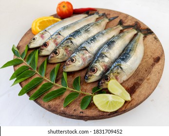 Fresh Indian Sardine Fish Decorated With Curry Leaves ,Lemon Slice And Tomatoes On A Wooden Pad ,White Background.